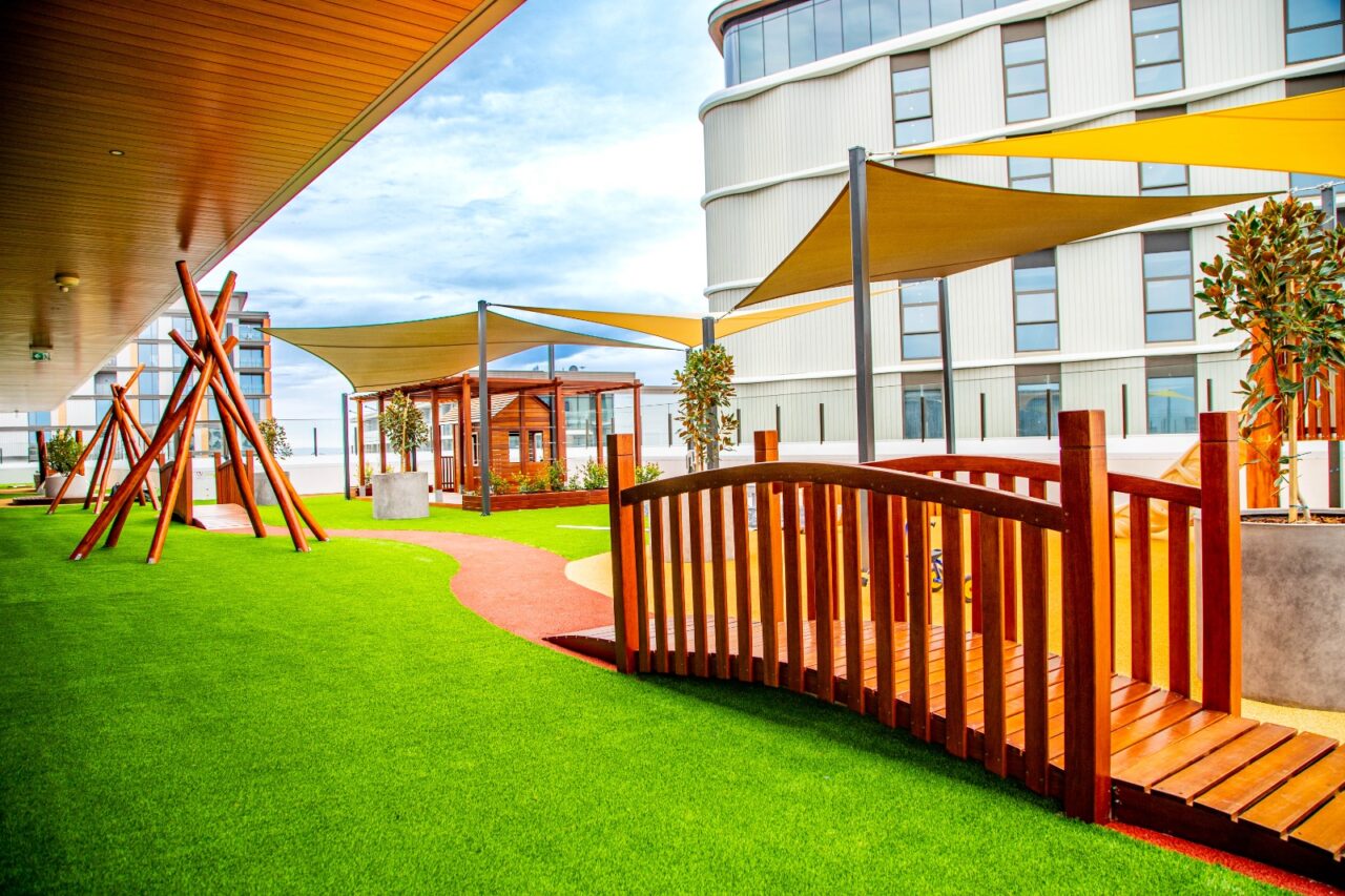 Level 5 rooftop playspace with a timber bridge, raised garden beds and artificial grass at Nurture Early Learning Murdoch