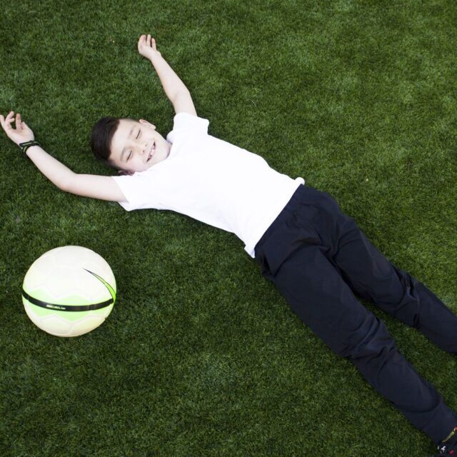 Child lying on an artificial grass lawn with a soccer ball