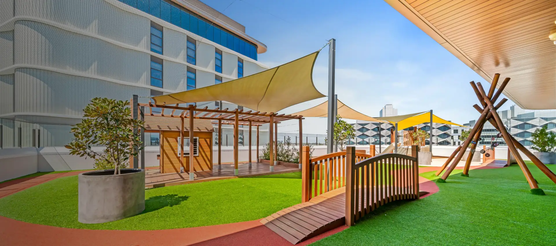 Rooftop playground in Perth with timber play structures, shade sails and artificial grass, built by Jays Playground Solutions