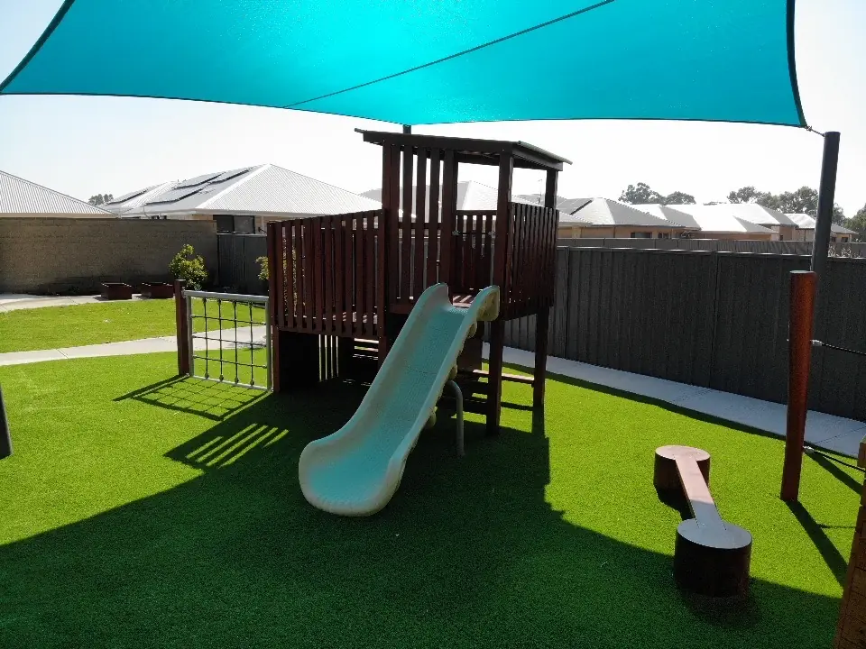 Artificial grass play yard with a timber climbing fort, slide and shade sail at Everwood Early Education, Forrestdale